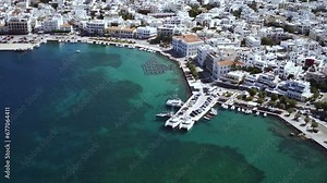 High drone footage of the cars driving on the coastal road with the cityscape of Tinos, Greece