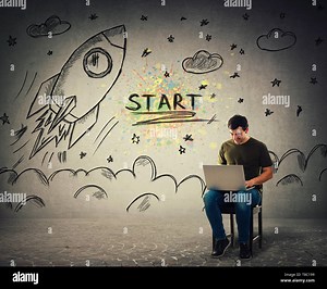 Creative young man freelancer working on laptop seated on a chair. Cheerful positive guy playing video games on his notebook computer as rocket ship s Stock Photo - Alamy