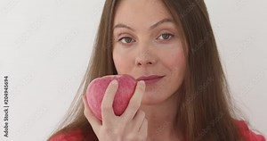 Young woman is eating a big red apple at white background. Healthy nutrition. Model eating fruit. Girl takes first bite and then offer bite to viewer and saying Wanna bite