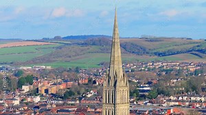 Telephoto aerial shot circling the spire of Salisbury Cathedral with the city in background