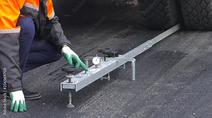 Inspection and testing of asphalt concrete pavement. A road construction site: A worker using a transport engineering instrument.