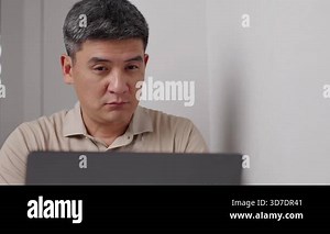 Exhausted businessman sits at laptop, takes of glasses and rubs reddened eyes. Tired manager in glasses sitting at home works remotely and focused on completing a task. Man wipes eyes after hard day.