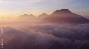 Epic sunrise drone flight at cloud level over San Pedro la Laguna around Atitlan Lake in Guatemala, with three volcanos visible in shot.