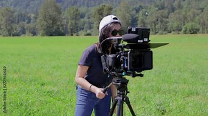 Woman operating a cinema camera on an open field