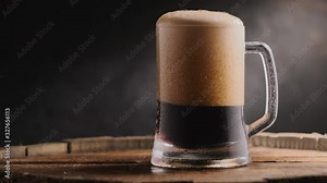 Cold dark beer in a beer mug on a dark background. A stream of cold beer is poured into a beer glass on a wooden barrel. 4K UHD footage