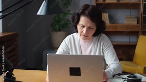 Confident stylish european middle aged senior woman using laptop at home. Stylish older mature 60s lady sitting at table looking at computer screen typing chatting reading writing email