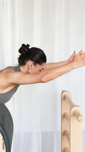 Pilates ladder barrel training machine. Active woman performing dynamic exercises on a Pilates ladder barrel machine using strong toned arm movements to engage full body muscles including core