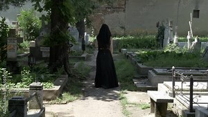 Creepy woman walking in cemetery alley to beloved grave and placing a crown on grave