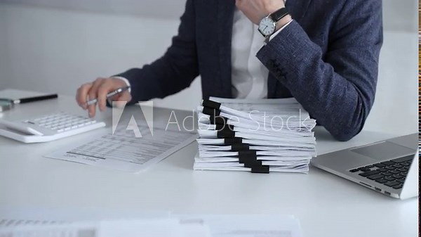 Business professional organizing documents at desk, managing paperwork and financial reports, working on taxes or corporate accounts with a laptop and calculator for audit preparation. Audit and taxes