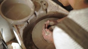 Slow motion, overhead view of a female potter beginning to open clay to form a vessel on a spinning wheel.