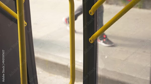 Close-up of opening yellow doors in a public city bus and unrecognizable people entering inside at a bus stop.