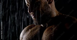 The face of a brutal bearded muscular male bodybuilder close-up on a black background, he is in the rain, water flows down him.
