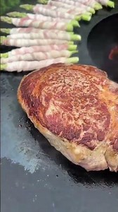 Grilling steak on a flat top grill with asparagus wrapped in bacon #popular #food #steak #grill