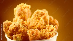 Rotation bucket full of crispy fried chicken on brown background. 4K video footage. Ultra high definition 3840X2160