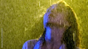 Wet female with bare neck and light-color clothes moves slowly in studio. Numerous drops of water fall on hair and body in blurry footage