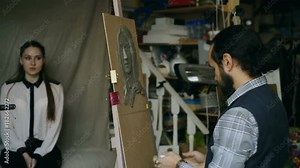 Sculptor creating sculpture of human's face on canvas while young woman posing to him in art studio