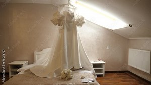 A beautiful white wedding dress hangs in the room. Preparation for the wedding ceremony.