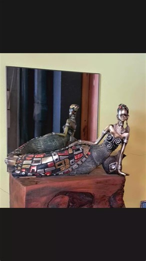 African-inspired collectible figurine of a woman, made of resin with a brushed bronze finish. The figurine depicts a woman in a reclining or sitting pose, adorned with jewelry and a detailed dress. The dress features eye-catching tribal designs with metallic accents in red, silver, and gold. It is a decorative art piece, often sold in sets, designed to enhance home decor with an African theme. #highlightsシ゚ #post #everyoneシ゚ | Justice Joy