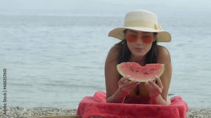 Woman eating watermelon.Beautiful woman in bikini with straw hat eats watermelon on the beach while sunbathing on a sunbed.