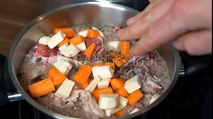 Person adding chopped parsnips to bone broth beginning to boil in pot.