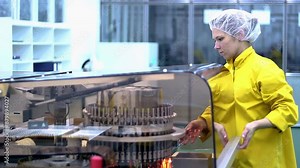 Female Production Line Worker Operates The Machine at Pharmaceutical Plant. Automated Visual Inspection Machine for Pharmaceutical Ampoules and Vials. Pharmaceutical Industry. Pharma Manufacturing.