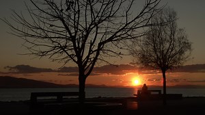 Download Lonely Woman Sitting on Bank Beach at Red Sunset in Winter And Looking Ocean for free