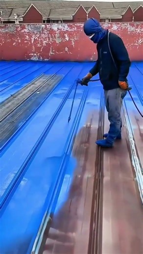 spraying blue paint on the metal roof to prevent rust and improve appearance of the building surface