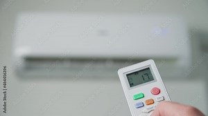 Hand adjusting temperature on air conditioner with remote control, Working air conditioner for comfort temperature in home at hot summer