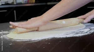A woman in an apron cooks in the kitchen, prepare the table and flour and knead the dough for the pie. Home cooking