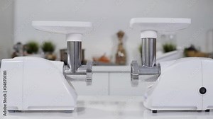 Two white electric meat grinders on white table in kitchen at home. Electric mincer machine for fresh chopped meat. Preparation of minced beef with an electric meat grinder. Dolly shot