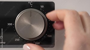 Woman adjusting modern white oven in kitchen. Female hand pushing and turning knobs on oven control panel. Closeup