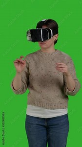 Vertical video: Front view close up of modern person having fun with vr glasses on greenscreen backdrop, using virtual reality headset with artificial intelligence. Woman enjoying interactive 3d
