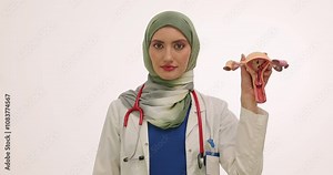 Female Muslim doctor holds colored condom pack and model of uterus. Lady in hijab encourages to use contraception against unexpected pregnancy slow motion