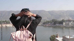 Handheld woman takes selfie photo video with her mobile cellphone device from a panoramic vantage view point of holy Pushkar lake, a sacred city for Hindu pilgrims mela festival bathing ghats temples
