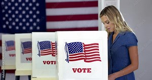 MS Young blonde woman enters and casts votes at booths in polling station with US flag. Locked off, slow motion 4K 60fps