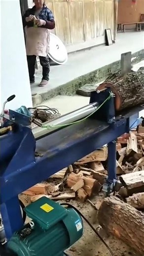 Operating electric log splitter machine for cutting firewood in a workshop area with pile of wood