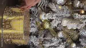 Vertical video of woman is preparing for the xmas holiday and placing gift boxes wrapped in festive gold paper under a luxury decorated Christmas tree. Creative pyramid of winter present for new year.