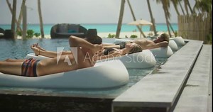 Three Beautiful Young People Sunbathing on the Deck Chairs in the Pool