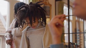 Girl looks down on table, talks, woman on background, touches head of girl, girl looks up and down again. Woman in front eats.