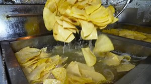 Quartered taco shells are being deep-fried to a golden crisp in a stainless steel fryer.