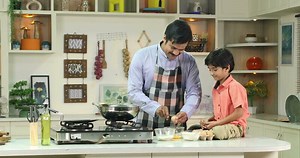 Dad and son in kitchen father teaches child to break eggs into a bowl cooking