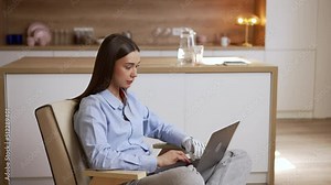 Young female freelancer is working with laptop and sitting in chair in home office spbas. 4k Close view of beautiful european woman with bionic prosthesis types on keyboard and browses web, does work