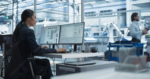 Asian Software Developer Managing a Cloud Computing Neural System on a Desktop Computer. Female Working in a Modern Technological Facility with an Automated Production Line with Robotic Arms