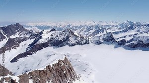 Beautiful cinematic aerial of snowy alpine mountain glacier peaks. Valleys and steep snow covered mountain ranges in distance. Drone flying forward, sunny day amazing landscape scenery view 4K