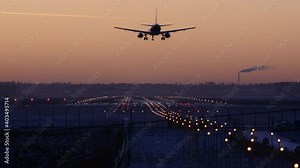 Cinematic footage of an evening landing of a commercial airplane on the airport runway. Passenger aircraft flies over airport landing lights