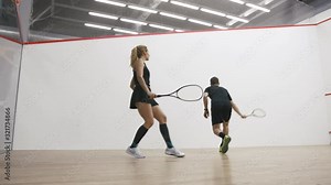 Young athletic man and woman play squash together in the squash court, slow motion, low angle view