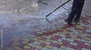 Washing paving slabs with a high pressure washer. Spring cleaning. A man in a navy blue uniform cleans dirt from paving slabs with a pressure washer.