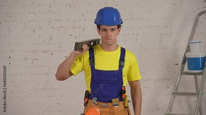 Medium video of a smiling young construction worker wearing a tool belt placing a construction water level on his shoulder and smirking.