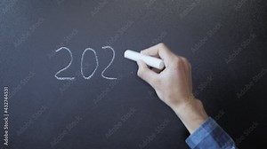 Writing 2021 plan on chalkboard. Hand writes PLAN 2021 in chalk on blackboard