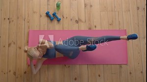 Top view of active motivated beautiful sporty fit mature female practicing bicycle crunches exercise on yoga mat, flexing and strengthening abdominal muscles and slimming waist during indoor workout.